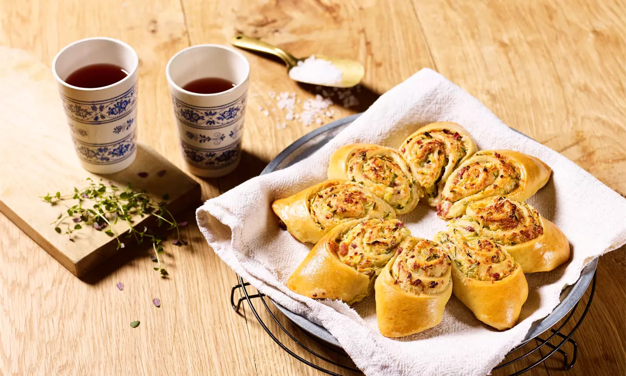 Feuilletés dorés en forme de spirales, garnis de légumes et d'herbes, disposés en étoile sur un linge blanc dans un plat en métal