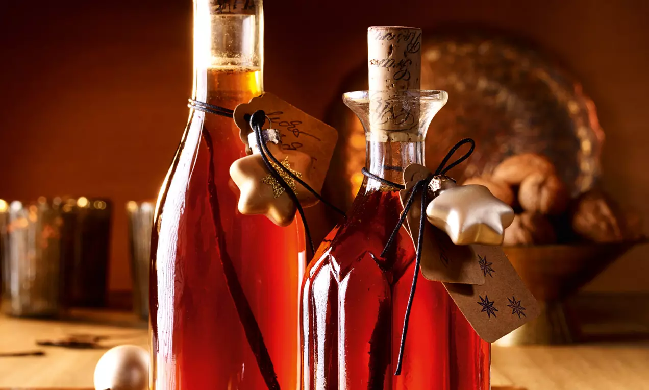 Liquore ambrato in eleganti bottiglie di vetro con tappi di sughero, decorato con etichette e nastri, su tavolo illuminato da luce calda