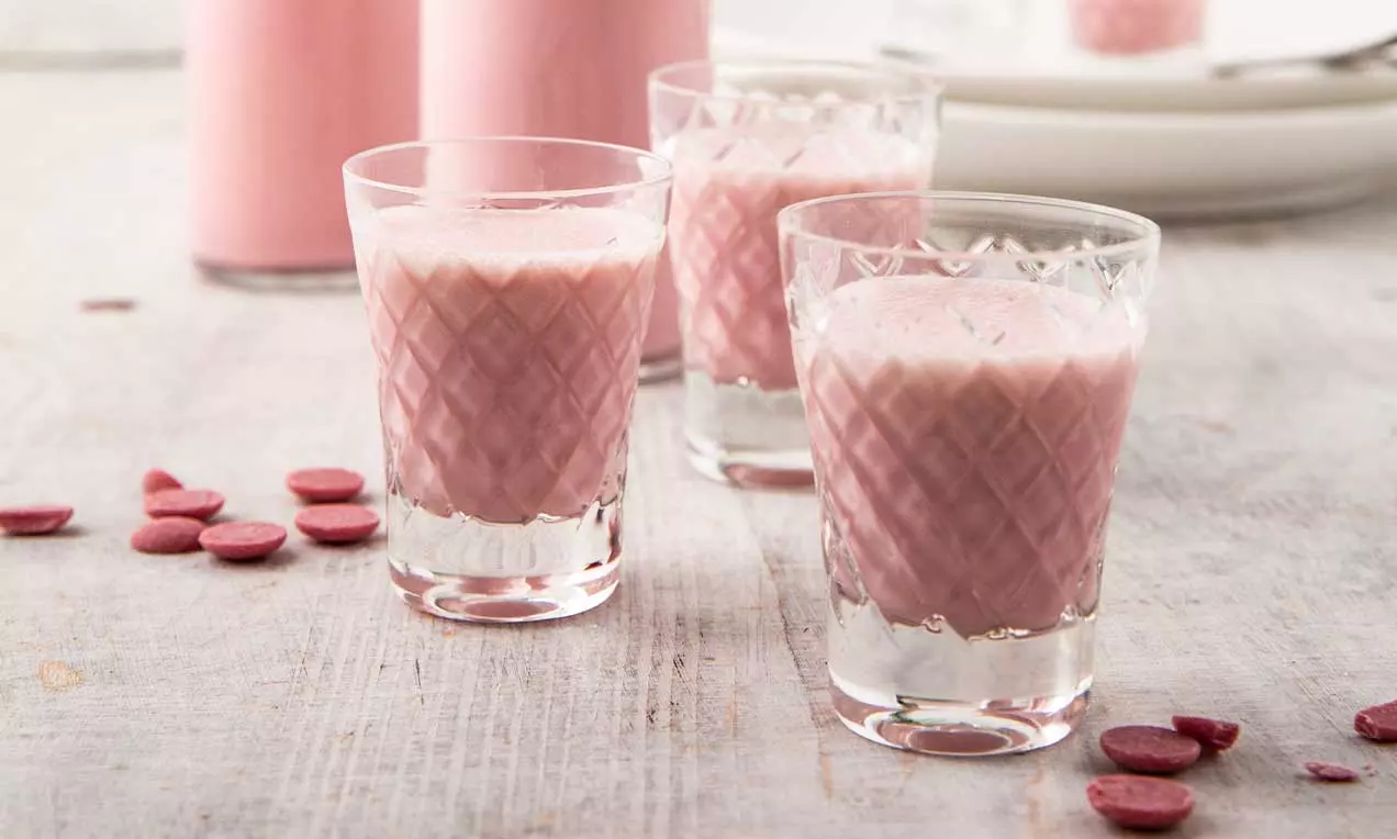 Bicchierini di liquore rosa cremoso con texture vellutata, decorati da un motivo intagliato su vetro e circondati da petali di cioccolato